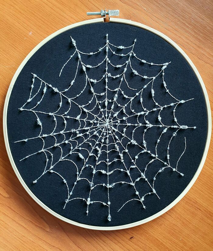 An intricate spiderweb embroidery creation made with white beads on a black fabric background.