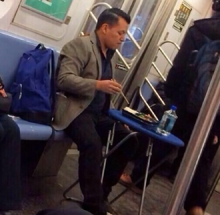 Man eating with chopsticks at a folding table inside a NYC subway car during a weird subway moment.