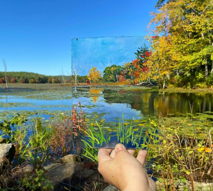 Hand holding a painting that perfectly matches the vibrant lake and autumn trees in the incredible real landscape.
