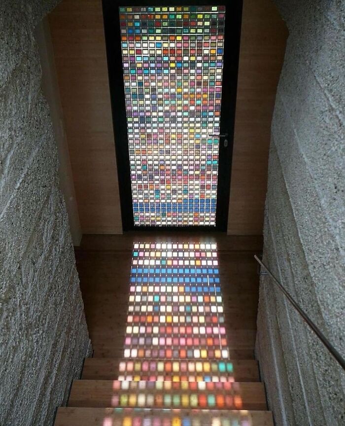 Colorful stained glass door casting vibrant patterned light on wooden stairs in a reality glitch illusion photo.