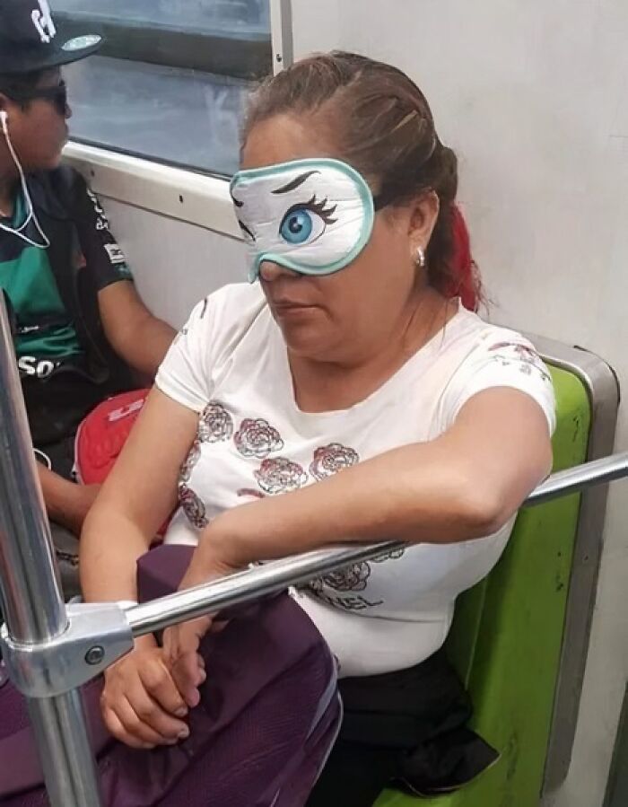 Woman wearing a quirky eye mask with a cartoon eye while sitting on a subway, capturing weird moments on the subway.