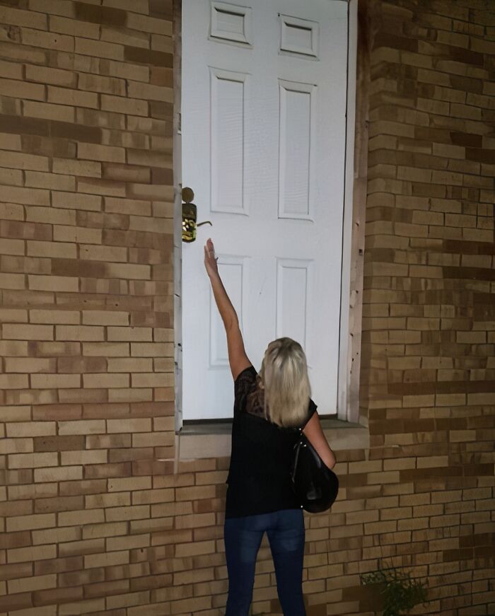 Woman reaching for a door handle on a door that leads absolutely nowhere against a brick wall.