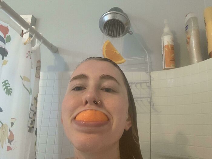 Person in shower with an orange slice in mouth and another orange slice under the showerhead, representing weirdest subreddits.