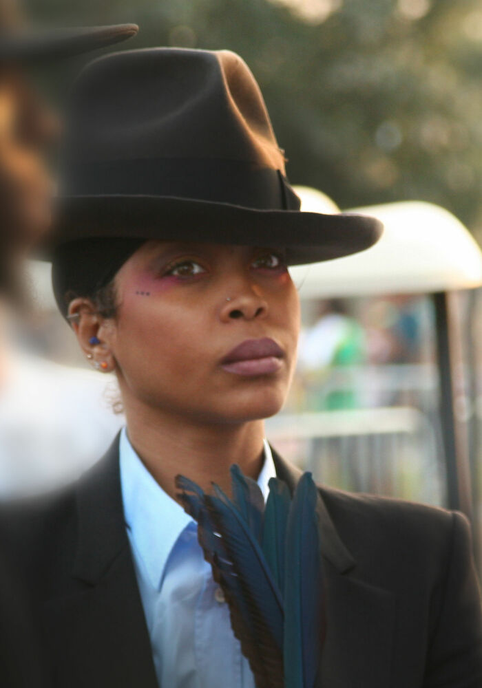 Erykah Badu wearing a black hat and suit jacket, showcasing her unique style in an outdoor setting.