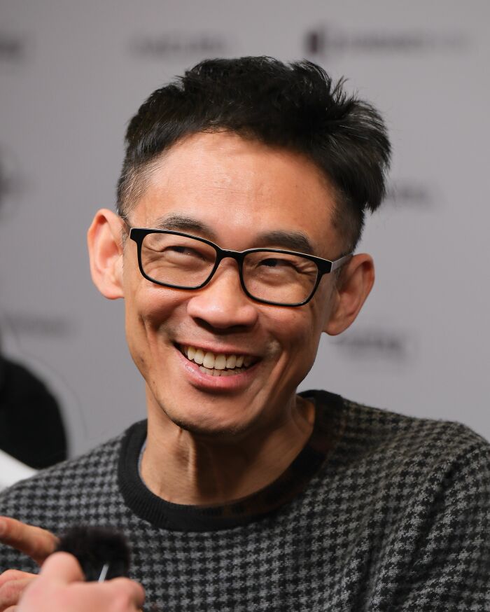 James Wan smiling and wearing glasses during an interview discussing his bio and career highlights.