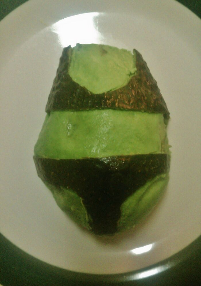 Half-peeled avocado with skin arranged to resemble a bikini top and bottom on a white plate, weirdest subreddits concept.