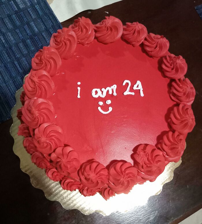 Red frosted cake with red swirls and white icing text i am 24 smiley face on a dark wooden table, weird subreddits theme.