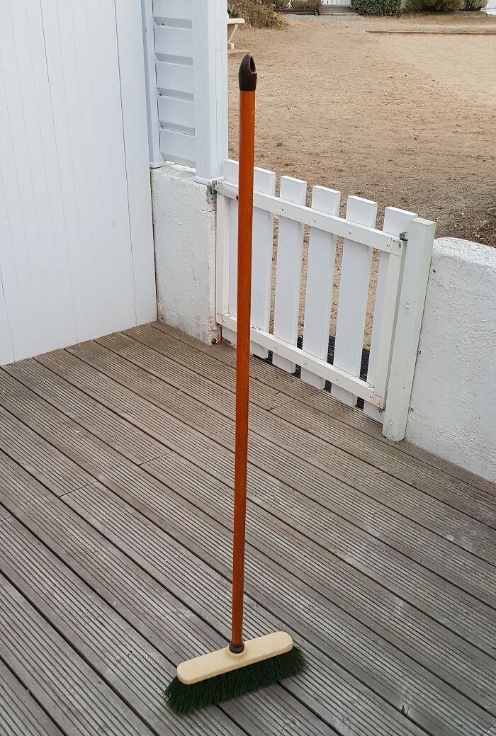 Broom standing upright on a wooden deck next to a white fence, representing weirdest subreddits popular topic.
