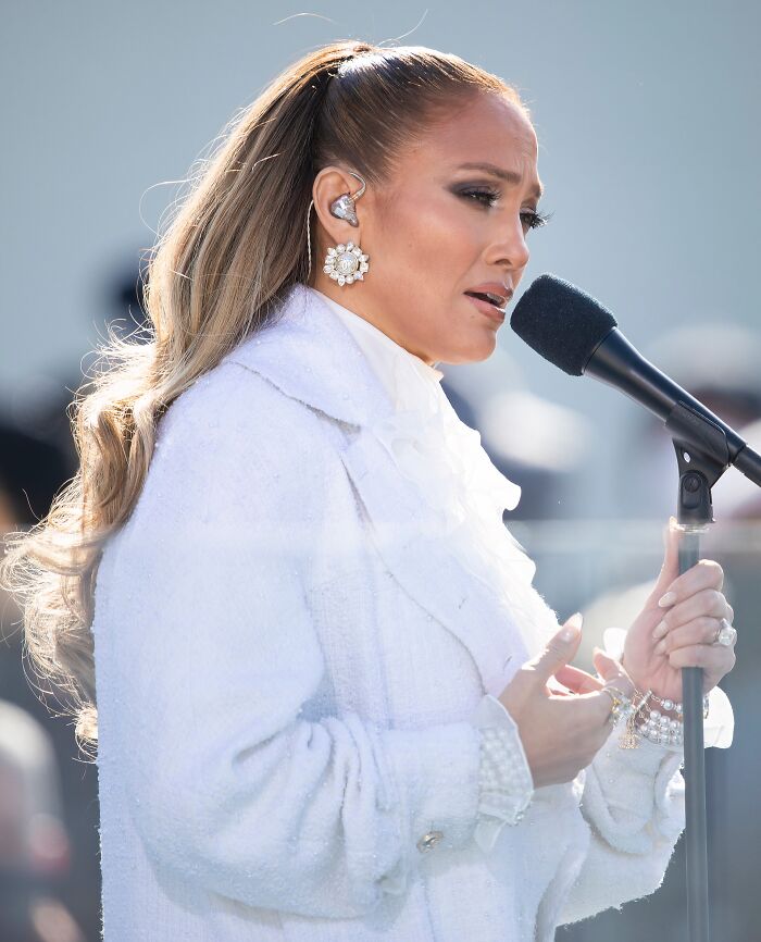 Female celebrity singer performing live, wearing white outfit and large earrings, highlighting luxury and mobile mansion lifestyle.