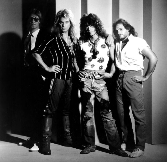 Black and white photo of four men posing with 1980s rock style, unrelated to custom $2.5 million mobile mansion concept.
