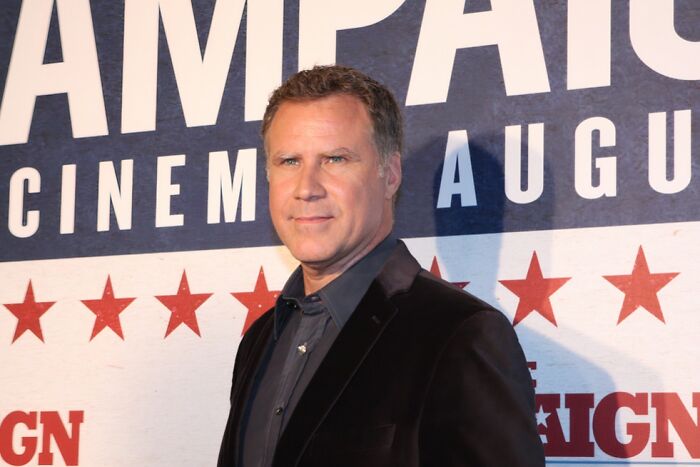 Actor in a black jacket at a cinema event backdrop featuring red stars and large text promoting a film.