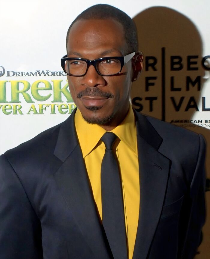 Man wearing black suit and yellow shirt with glasses at a film festival event about a custom $2.5 million mobile mansion.