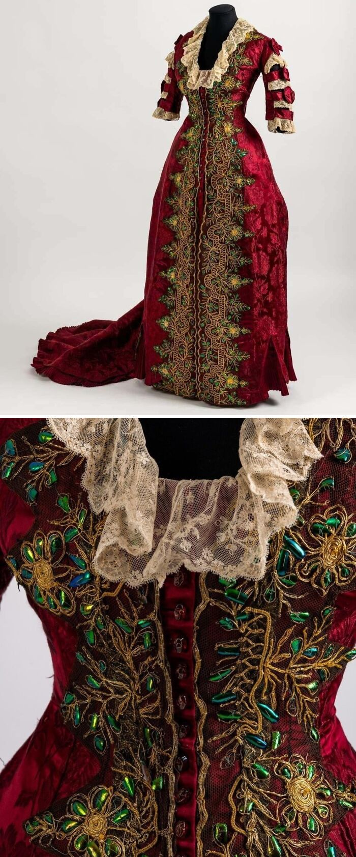 Red historical garment with intricate gold and green embroidery and lace collar on a black mannequin.
