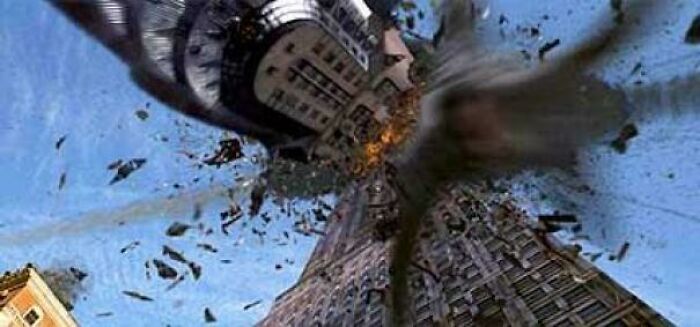 A building exploding into pieces, debris flying through the air against a blue sky, an example of nonsensical movie details.