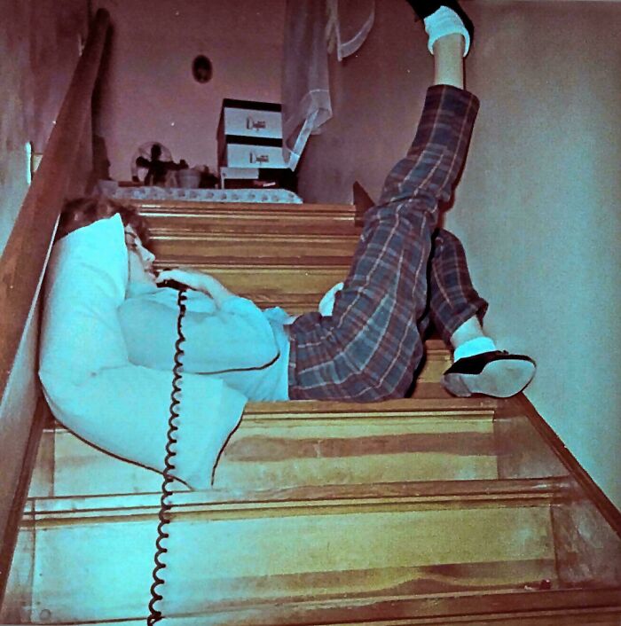 A candid old photo of a person lying on stairs talking on a corded phone, generations ago.