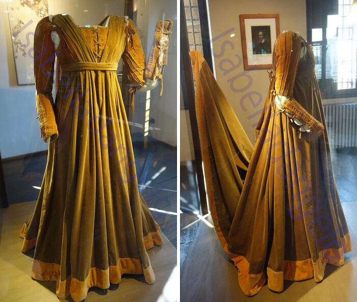 Vintage golden historical garment displayed in museum, showcasing detailed sleeves and flowing fabric from past centuries.