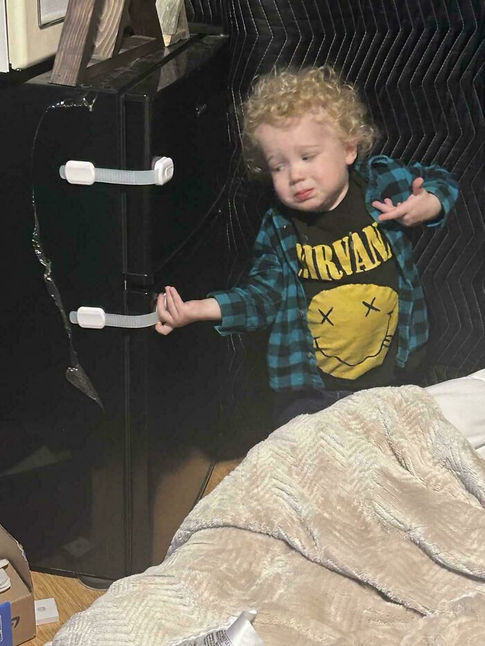A toddler gesturing dramatically by a refrigerator, looking like an accidental Renaissance figure.