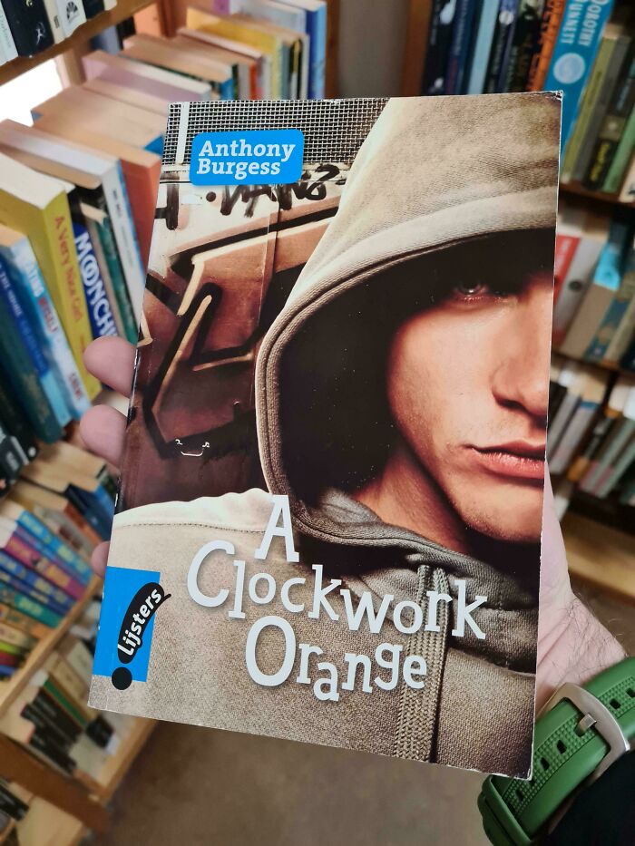 Book cover of A Clockwork Orange by Anthony Burgess featuring a close-up of a person in a hoodie, among other books on shelves.