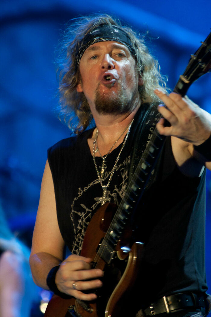Adrian Smith playing guitar on stage wearing a bandana and black sleeveless shirt during a live performance.