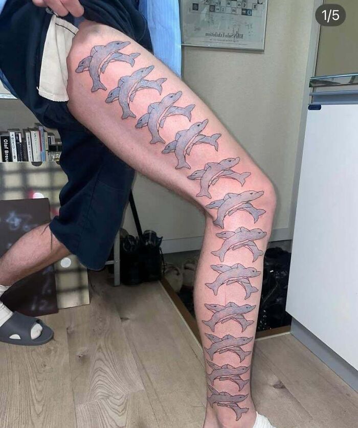 Tattoo of multiple dolphins covering a person's leg, an example of terrible tattoos marked by poor design choices.