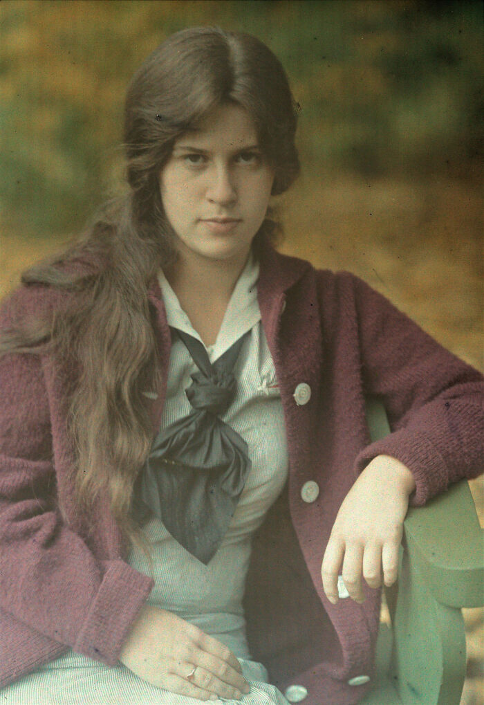 A candid old photo of a young woman with long hair, wearing a purple cardigan, generations ago.