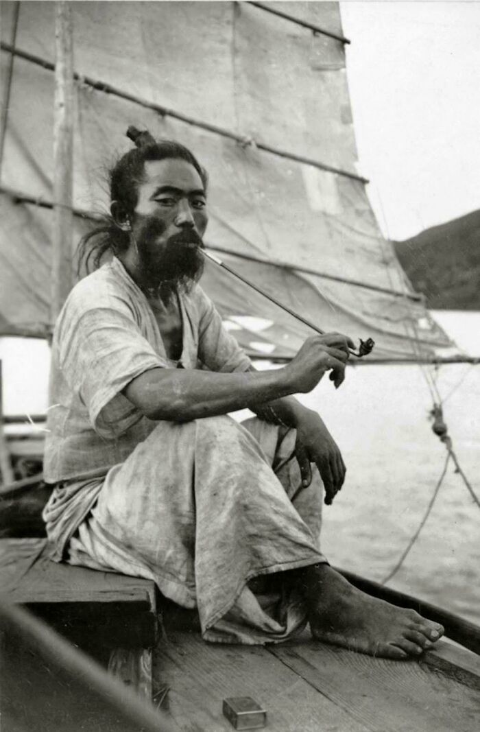 A candid old photo of a man with a beard smoking a pipe on a boat, showcasing generations ago.