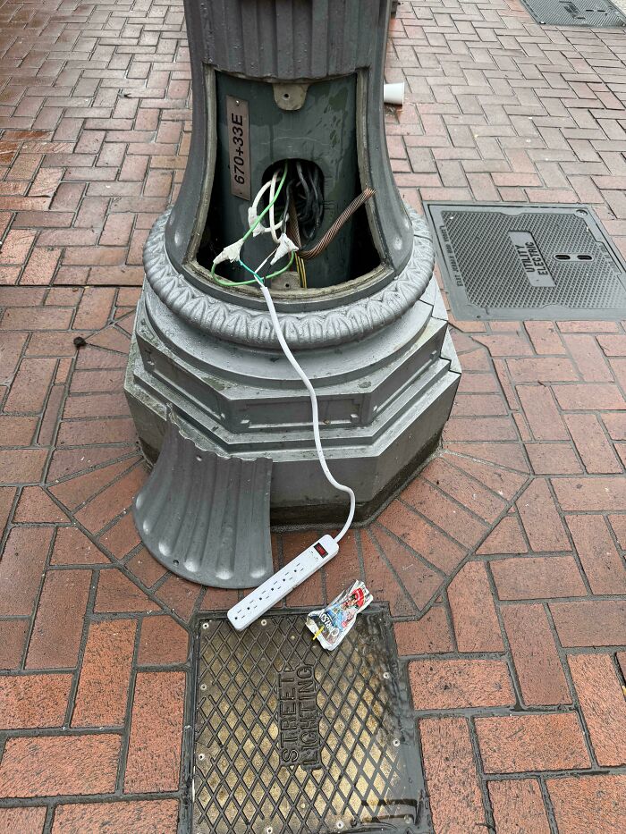 Exposed electrical wiring with a power strip connected inside a broken streetlight base, a risky example of redneck engineering.