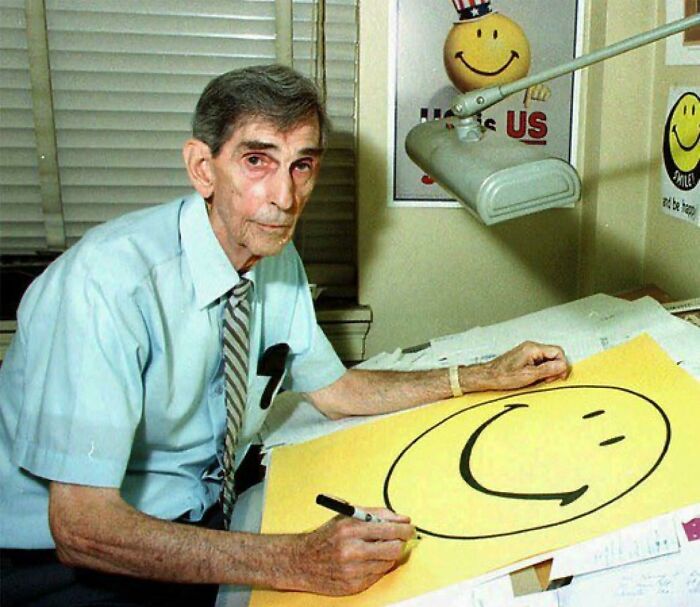 Elderly man drawing iconic smiley face, representing rare and intriguing photos that reveal history between the headlines.