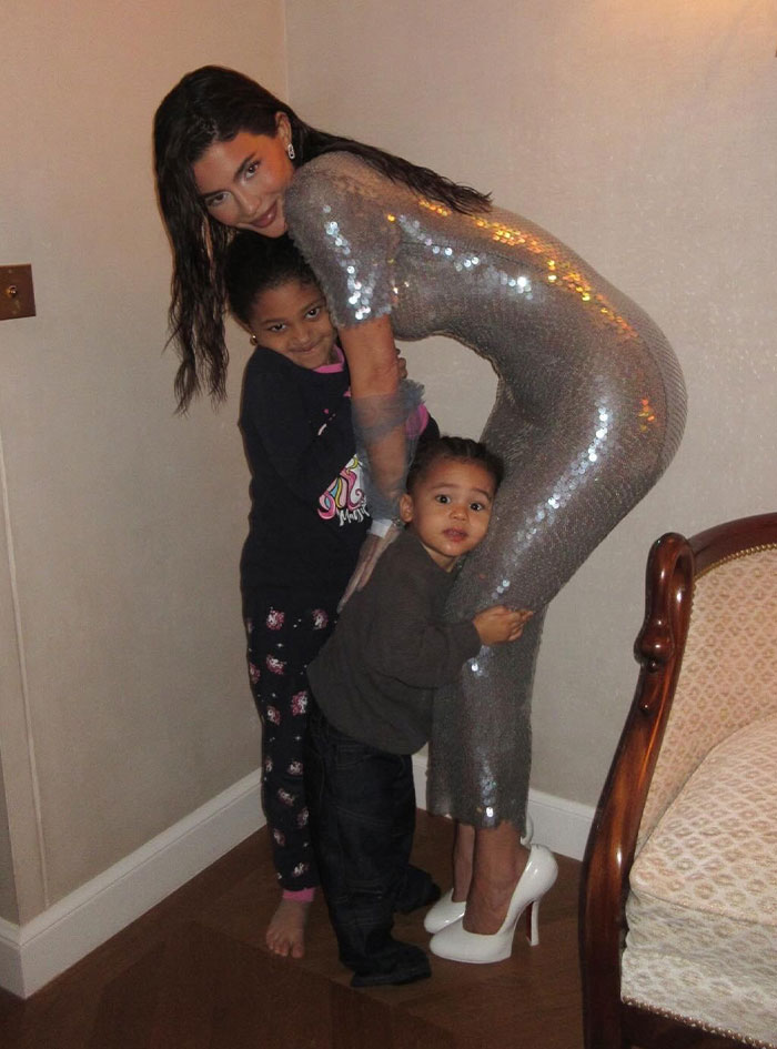 Kylie Jenner posing with two children at a party, related to Travis Scott and Kylie Jenner kids birthday party controversy.