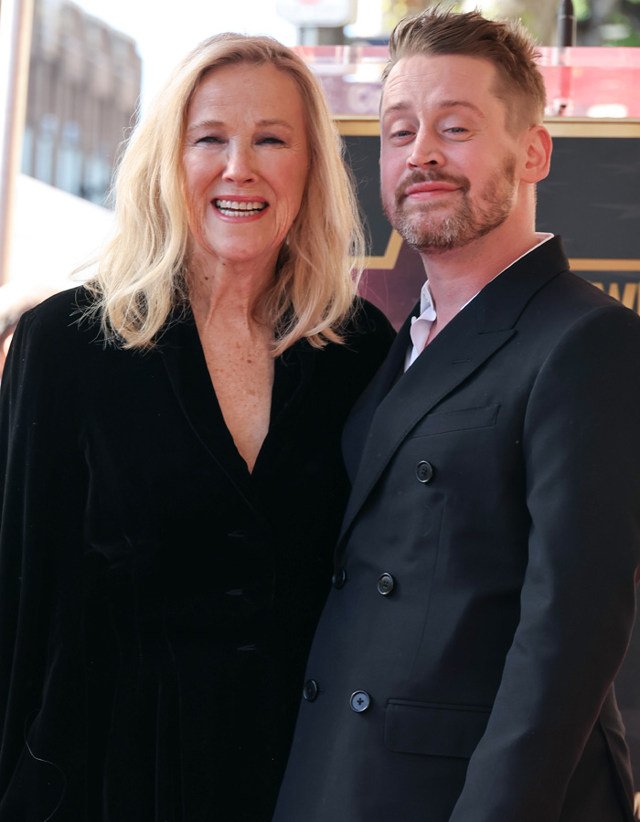 Catherine O'Hara smiling with a man in a black suit, discussing the cause of Catherine O'Hara's passing revealed.