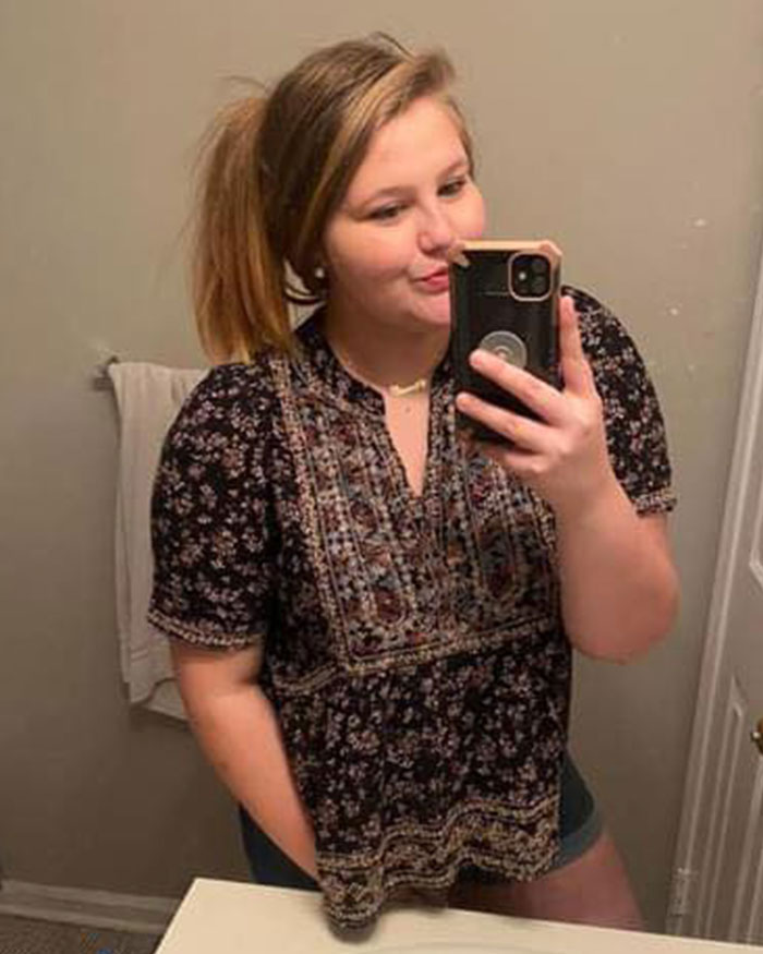 Young vet tech taking a mirror selfie indoors, wearing a patterned shirt, highlighting vet tech charged and fired news.