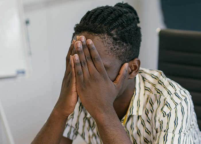 Man with braided hair covering his face in frustration, illustrating relatable today I messed up stories to feel better.