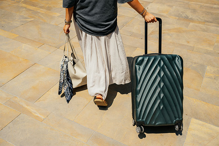 Woman walking with suitcase and handbag on sunny pavement, representing woman marrying weeks after meeting husband.