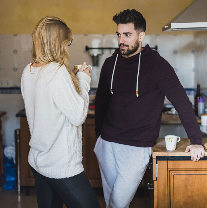 Man and woman having a serious conversation in a kitchen about family needing to move in with them.