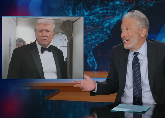 Jon Stewart on a talk show set reacting to a video clip, discussing Epstein files and his name emerging in reports.