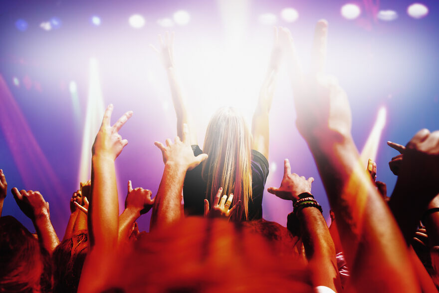 Crowd enjoying a lively concert with hands raised, capturing the energy of cities where sleep is optional nightlife.