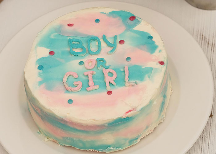 Gender reveal cake with boy or girl written in pink and blue icing, decorated with colorful sprinkles on a white plate