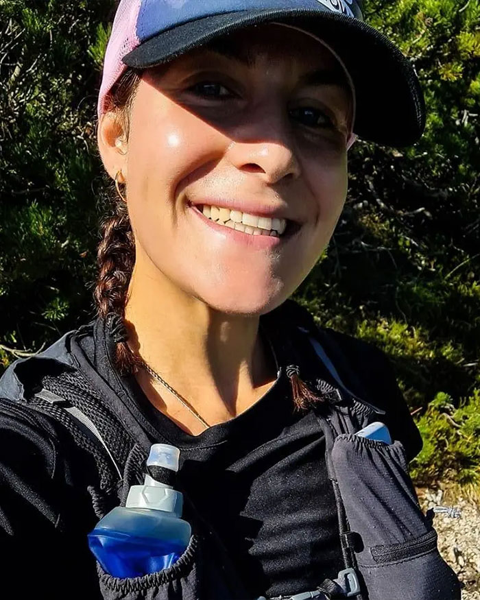 Smiling female climber outdoors wearing a cap and hydration pack, linked to climber revealing girlfriend's heartbreaking last words.