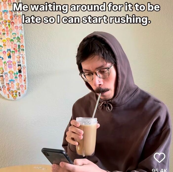 Man in glasses and hoodie sipping iced coffee while looking at phone, showing cynicism in a hilarious meme.