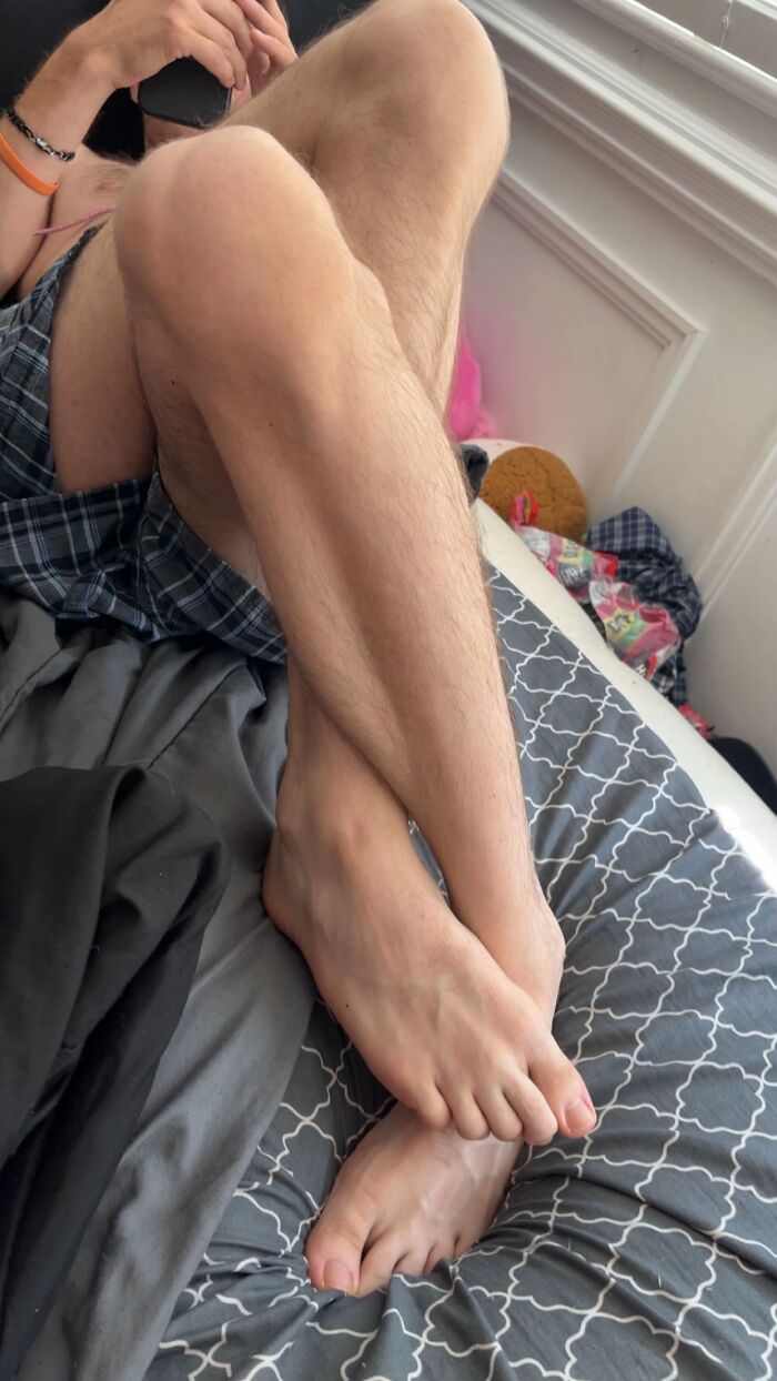 Close-up of a man’s awkward body language sitting cross-legged on a bed, showing legs and feet in a casual pose.