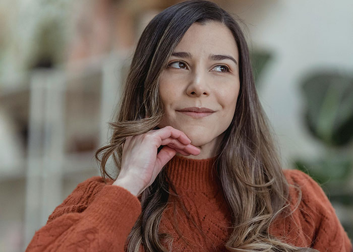 Young woman in an orange sweater reflecting quietly, symbolizing teen ensuring stepmom is miserable on her wedding day.