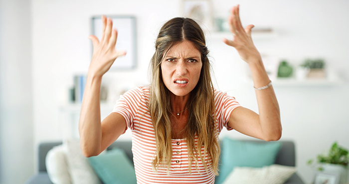 Frustrated woman indoors raising hands, representing psychiatric nurse turned psychiatric patient after secret revealed.