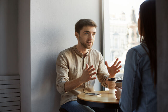 Man expressing a brutal wake-up call while talking to a woman across a table in a bright cafe setting