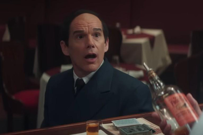 Man in a dark suit reacting surprised at a bar with a glass and bottle, scene from Oscar nominated movies 2026.