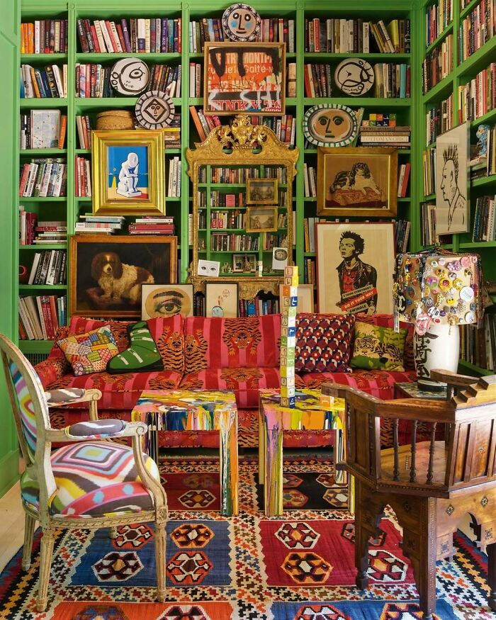 Vibrant bold and beautiful interiors with eclectic furniture, colorful art, patterned rug, and green bookshelves filled with books.