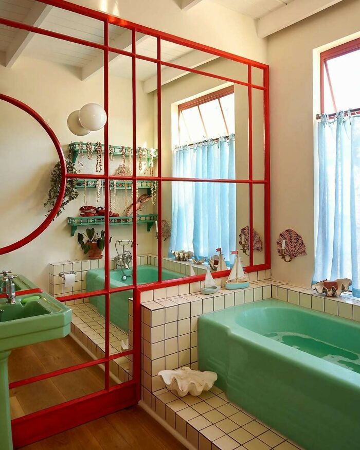 Green bathtub and sink in a bold and beautiful interior with red framed mirror and blue curtains in a stylish bathroom design