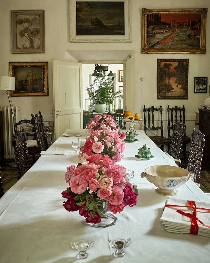 Elegant dining room with bold and beautiful interiors featuring vintage furniture, floral centerpiece, and classic paintings on walls.