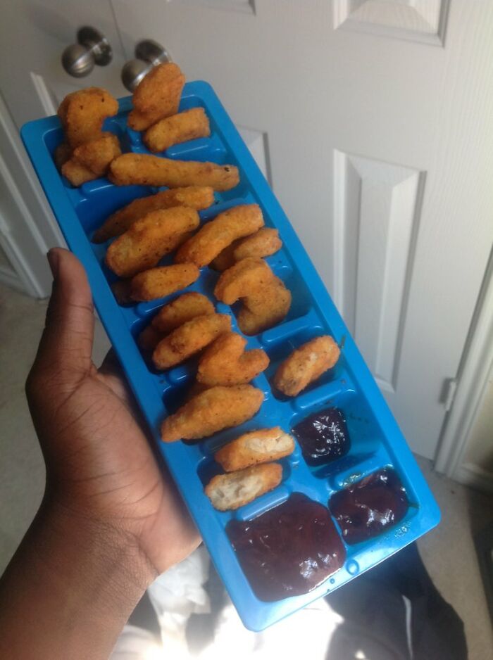 Chicken nuggets arranged in an ice cube tray with barbecue sauce, showing a lazy and creative snack setup.