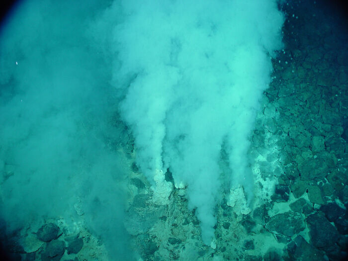 Underwater ocean vents releasing plumes of steam amidst rocky ocean floor in an unexpected ocean photo.