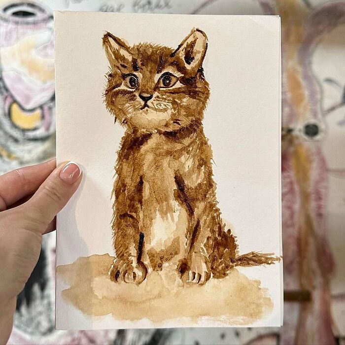 Watercolor painting of a brown cat held by a hand, showcasing cats as a favorite art subject through the years.